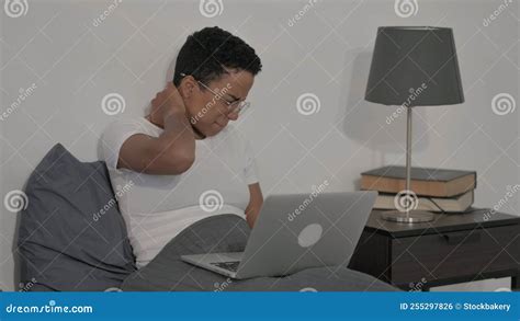 African Woman Having Neck Pain While Using Laptop In Bed Stock Photo