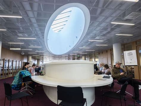 People Are Sitting At Tables In An Open Area With Bookshelves On The Walls