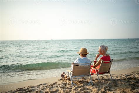 A Couple Of Elderly Sitting In Chairs At The Beach Watching The Sun And