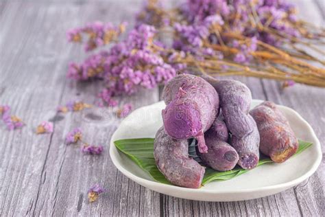 A Pile Of Ripe Purple Yams Is Placed On A Plate On A Wooden Table With Blurred Purple Flowers In