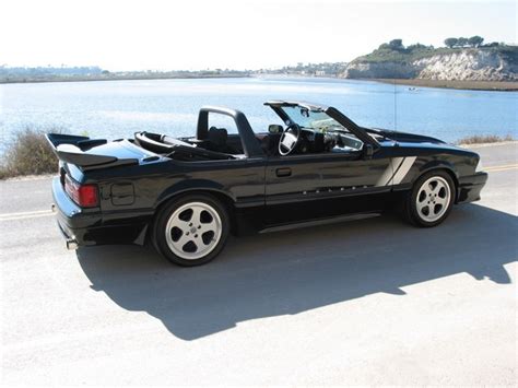 A Black Sports Car Is Parked On The Side Of The Road By The Water With