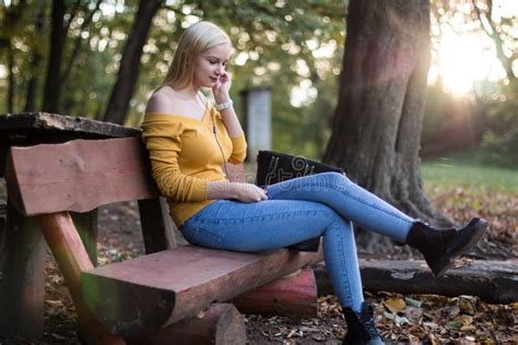 Jeune Femme Blonde S Asseyant Sur Un Banc En Bois En Parc Coutant La Musique Photo Stock
