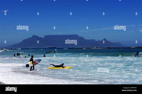 South African surfers at Bloubergstrand beach with a dramatic view of the Table Mountain in the ...