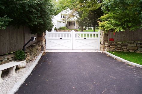 a driveway with a stone wall and white gate