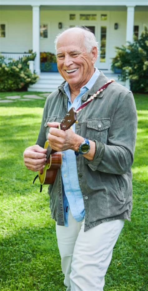 an older man standing in front of a white house holding a guitar and smiling at the camera