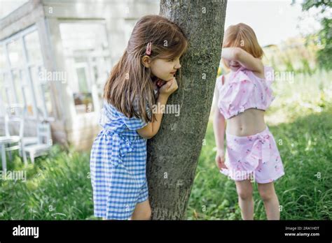 Small Kids Play Hide And Seek Outdoors In The Garden A Cute Girl Is