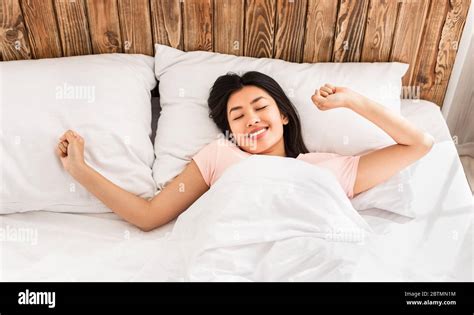 Korean Girl Waking Up Lying In Bed Stretching Hands Above View Stock