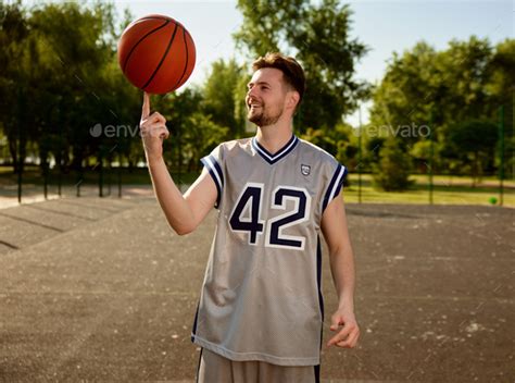 Man Spinning Basketball Ball On Finger Over Street Court Background