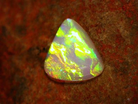 An Opalite Stone Sitting On Top Of A Red Rock With Green And Yellow Colors