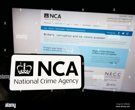 Person Holding Smartphone With Logo Of British National Crime Agency Nca On Screen In Front Of