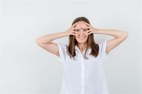 Mujer joven mirando a través de los dedos en blusa blanca y mirando