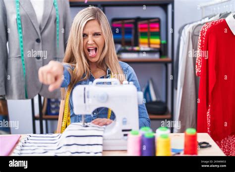 Blonde Woman Dressmaker Designer Using Sew Machine Pointing Displeased