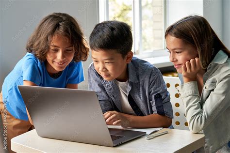 Diverse happy school kids using laptop computer together in classroom ...