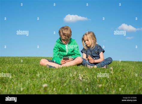 Gl Ckliche Blonde Kinder Mit Smartphone Film Oder Spiel Sitzen Auf Dem Rasen Bruder Und