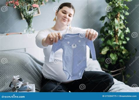 Pregnant Woman With Big Belly Holding Bodysuit And Sorting Clothes For