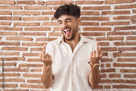 Arab Man With Beard Standing Over Bricks Wall Background Showing Middle Finger Doing Fuck You