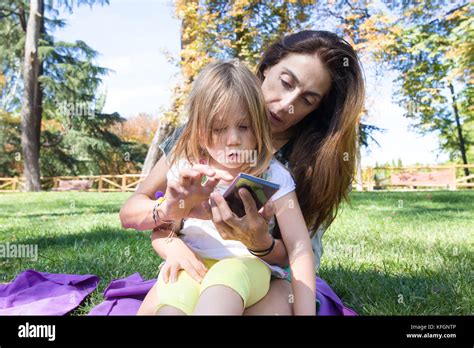 Four Years Age Blonde Girl With Surprise Face Sitting On Woman Mother Legs Watching