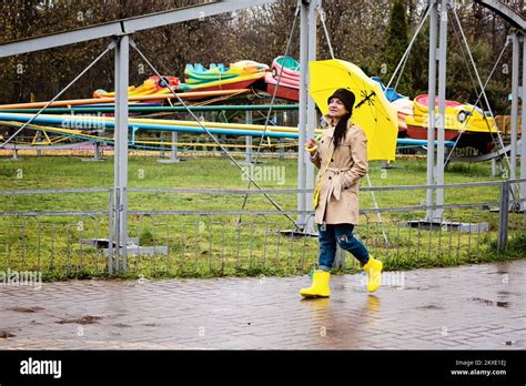 Happy Senior Woman In Yellow Rain Coat With Yellow Umbrella Walking In