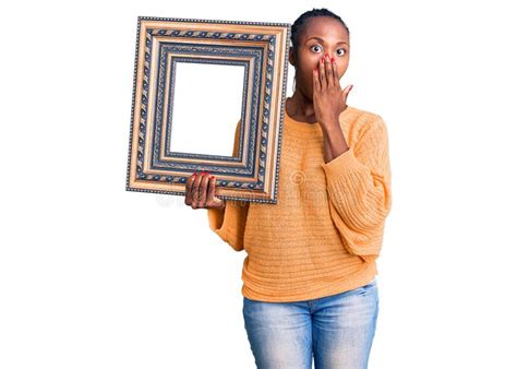 Young African American Woman Holding Empty Frame Covering Mouth With Hand Shocked And Afraid