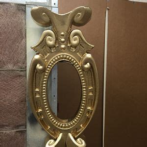 a gold mirror sitting on top of a counter next to a wall mounted toilet paper dispenser