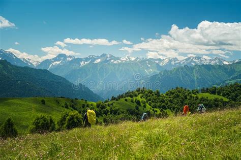 A Group Of Hikers With Capes On Their Backpacks Walking Down A Grassy