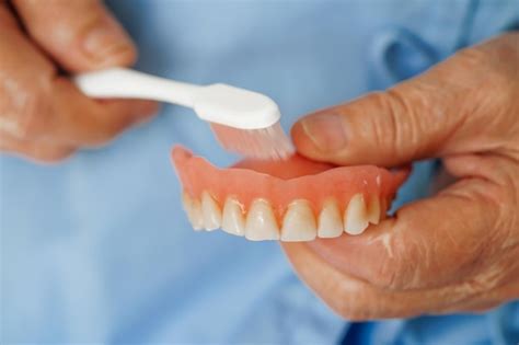 Paciente idosa asiática segurando dentadura de dentes na mão para