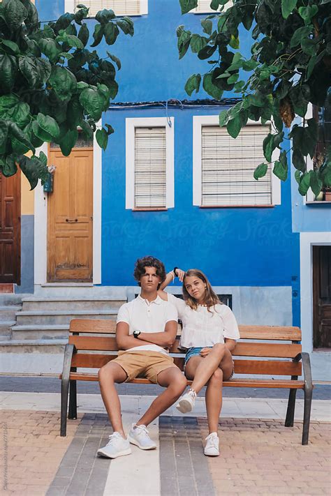 Vacation Portrait Of Teen Couple On A Bench In Front Of A Bright Blue