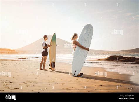 Surfers Couple Standing On The Beach With Surfboards Preparing To Surf