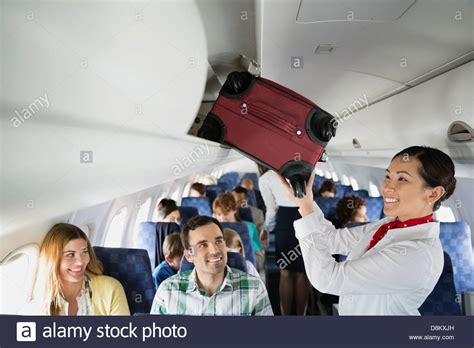 Flight Attendant Putting Luggage In Overhead Bin In Airplane Stock