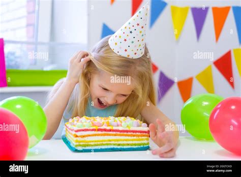 Blonde Caucasian Girl Peeking Out From Behind Birthday Cake With A Funny Face On Birthday Party