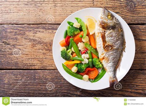 Plate Of Baked Fish With Vegetables On Wooden Table Stock Photo Image