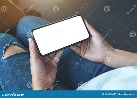 Woman`s Hands Holding Black Mobile Phone With Blank White Screen Horizontally In Cafe Stock