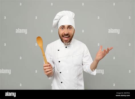 Emotional Mature Male Chef With Spoon On Grey Background Stock Photo