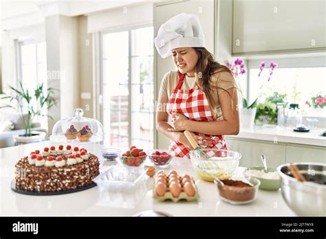 Beautiful Young Brunette Pastry Chef Woman Cooking Pastries At The Kitchen With Hand On Stomach