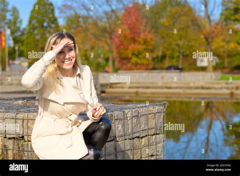 Attraktive blonde Frau mittleren Alters kniet an einem See und hält