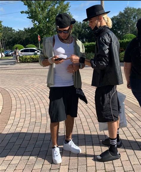 Two Men Standing Next To Each Other While Looking At A Cell Phone In