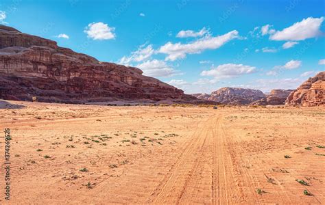 Rocky massifs on red sand desert, bright cloudy sky in background ...