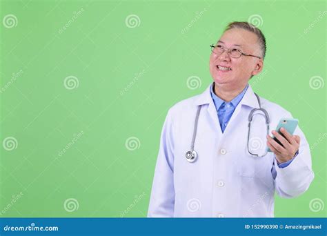 Happy Mature Japanese Man Doctor Thinking While Using Phone Stock Photo