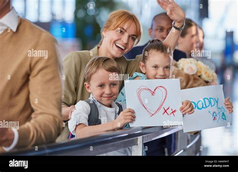 Mother And Children With Welcome Signs For Father At Airport Stock