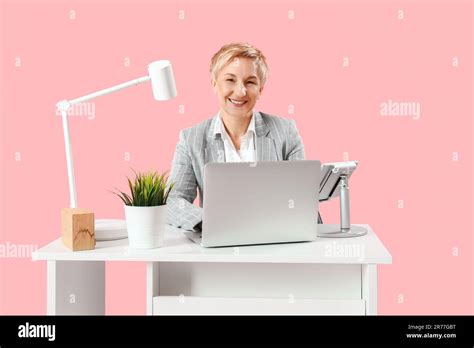 Mature Female Programmer Working With Laptop At Table On Pink