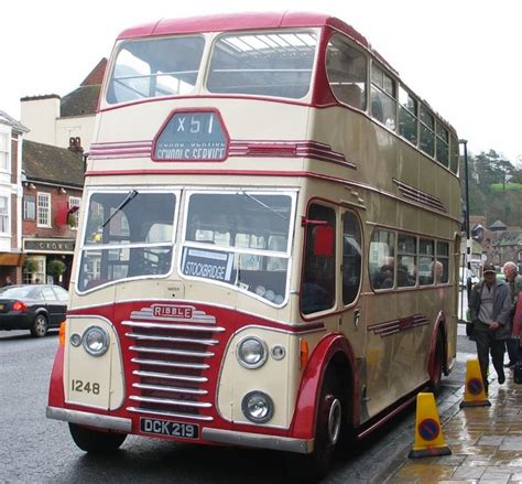 A Double Decker Bus Is Driving Down The Street In Front Of Some People