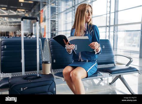 Stewardess With Suitcase Sitting On Seat In Waiting Area In Airport And