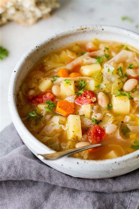 A White Bowl Filled With Vegetable Soup On Top Of A Gray Napkin Next To