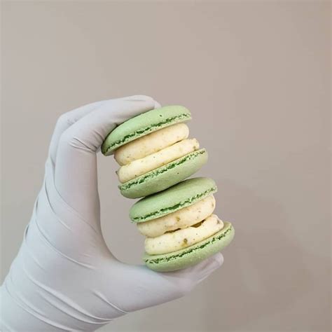 A Person In White Gloves Holding Up Some Green And Yellow Macaroons