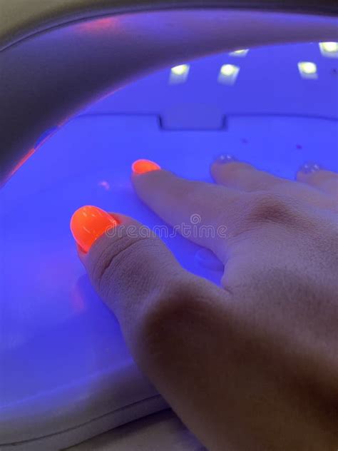 Female Hand With Neon Orange Manicure Inside A Blue Uv Lamp Drying Gel