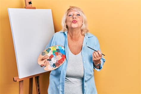 Middle Age Blonde Woman Standing Drawing With Palette By Painter Easel