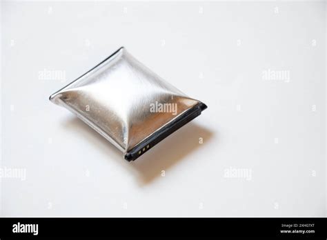 A Telephone Battery That Is Swollen From Overheating Lies On A White