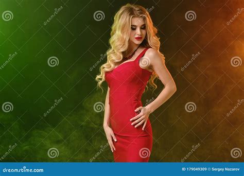 Curly Blonde Female With Alluring Decollete In Red Fitting Dress And Necklace Hand On Waist