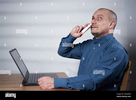 Mature Businessman Using Nasal Spray Or Inhaler At Work In Front Of