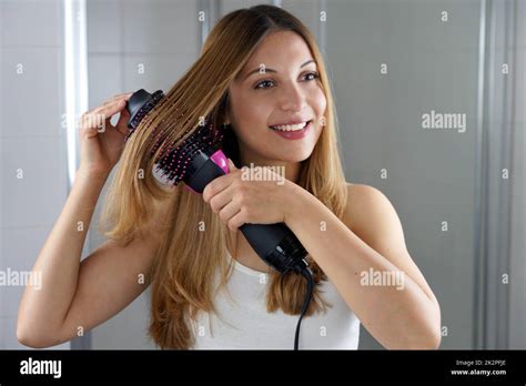 Young Woman Holds Round Brush Hair Dryer To Style Hair In An Easy Way